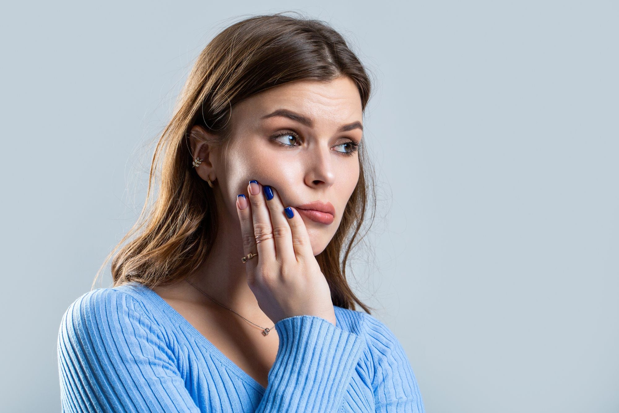 A woman wearing a blue sweater holds her chin, in pain due to to a cold sore.