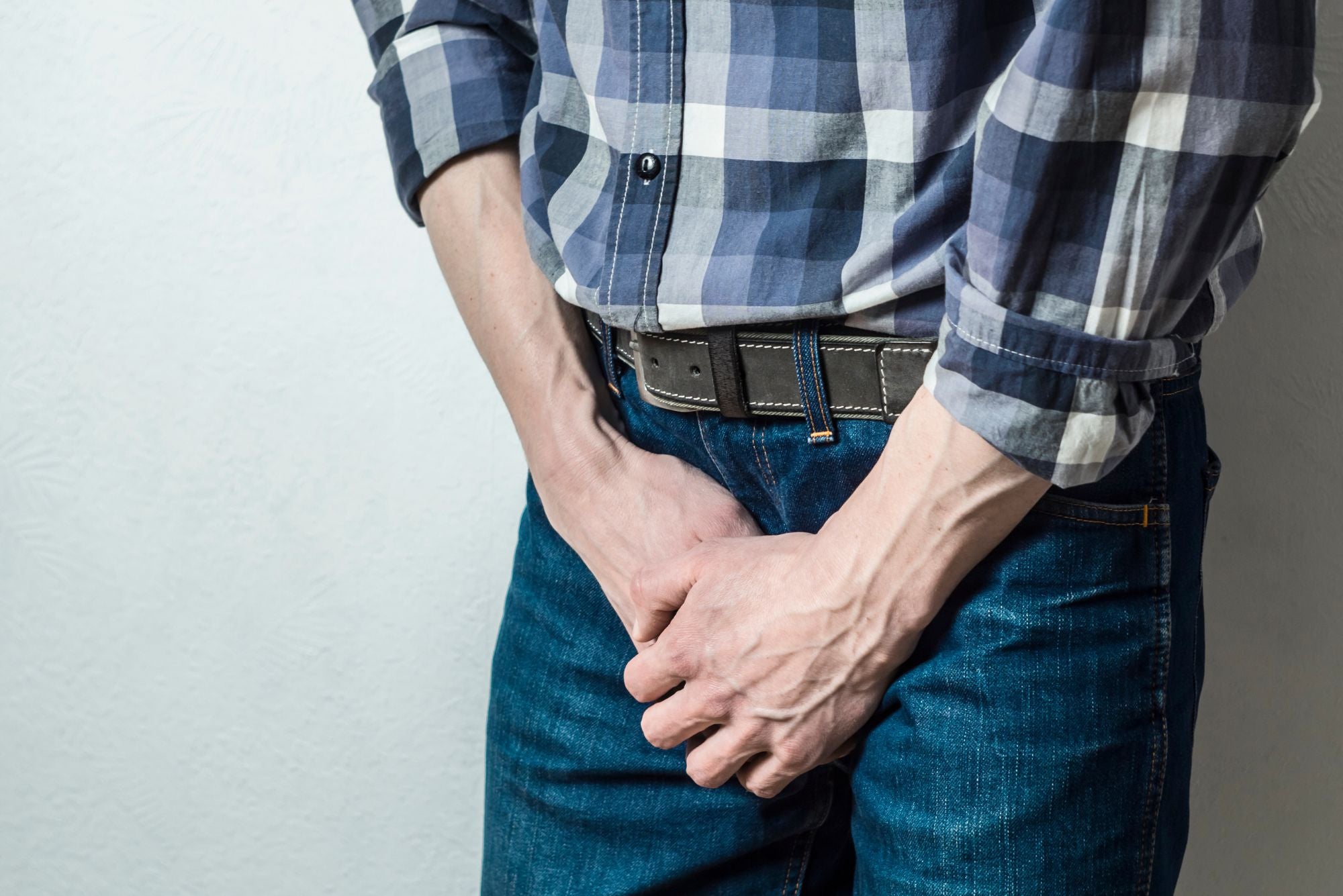 A man in a checkered shirt exhibits pain in the groin area while considering home remedies for genital herpes.