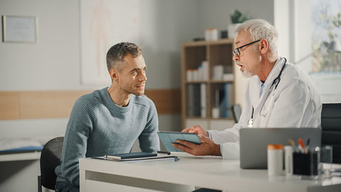 A doctor holding a tablet talks to a middle-aged man about herpes transmission.