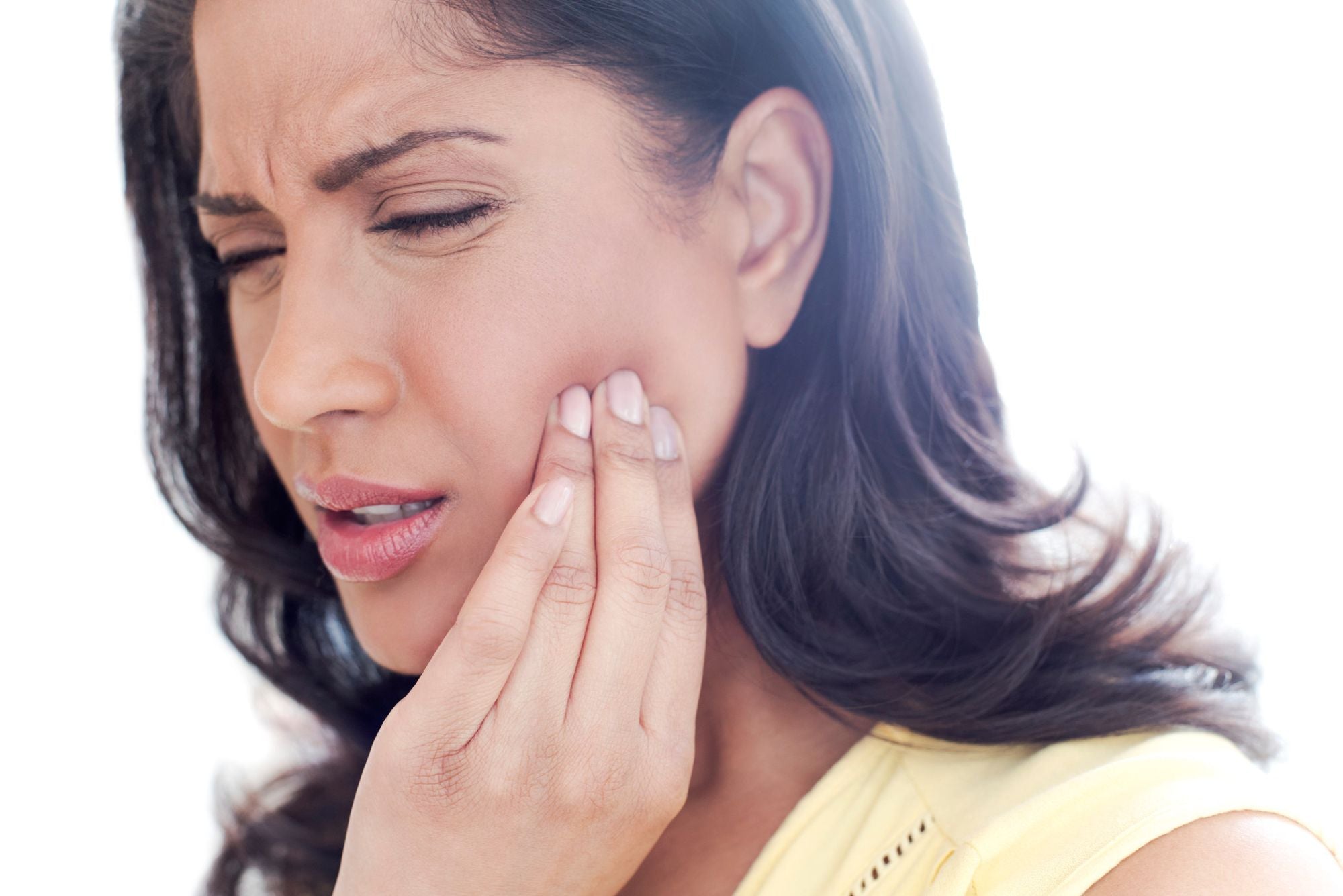 A woman holds her cheek in pain and cringes because of a canker sore.