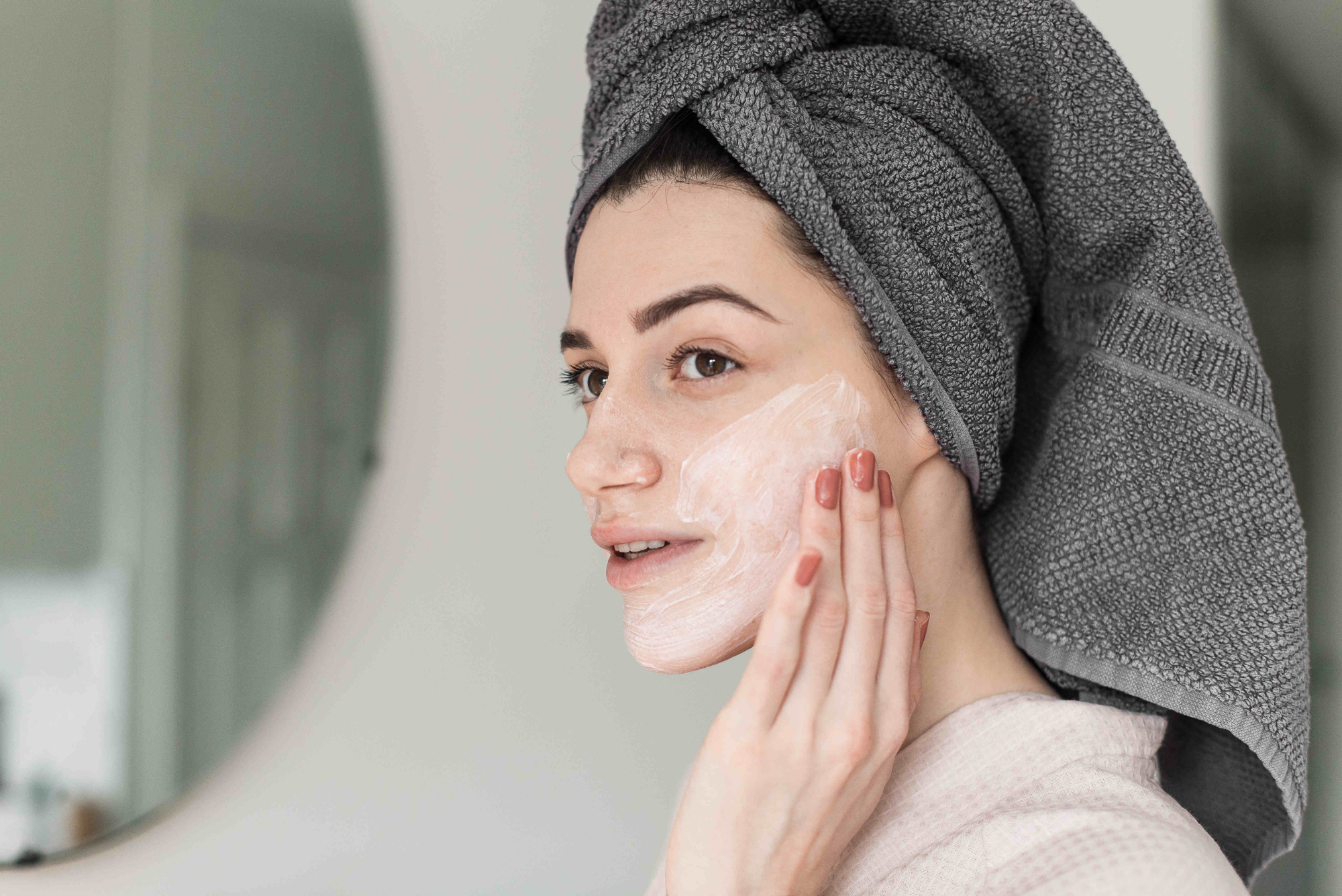 A woman with dark hair rubs her best red light therapy lotion on her face after a treatment.