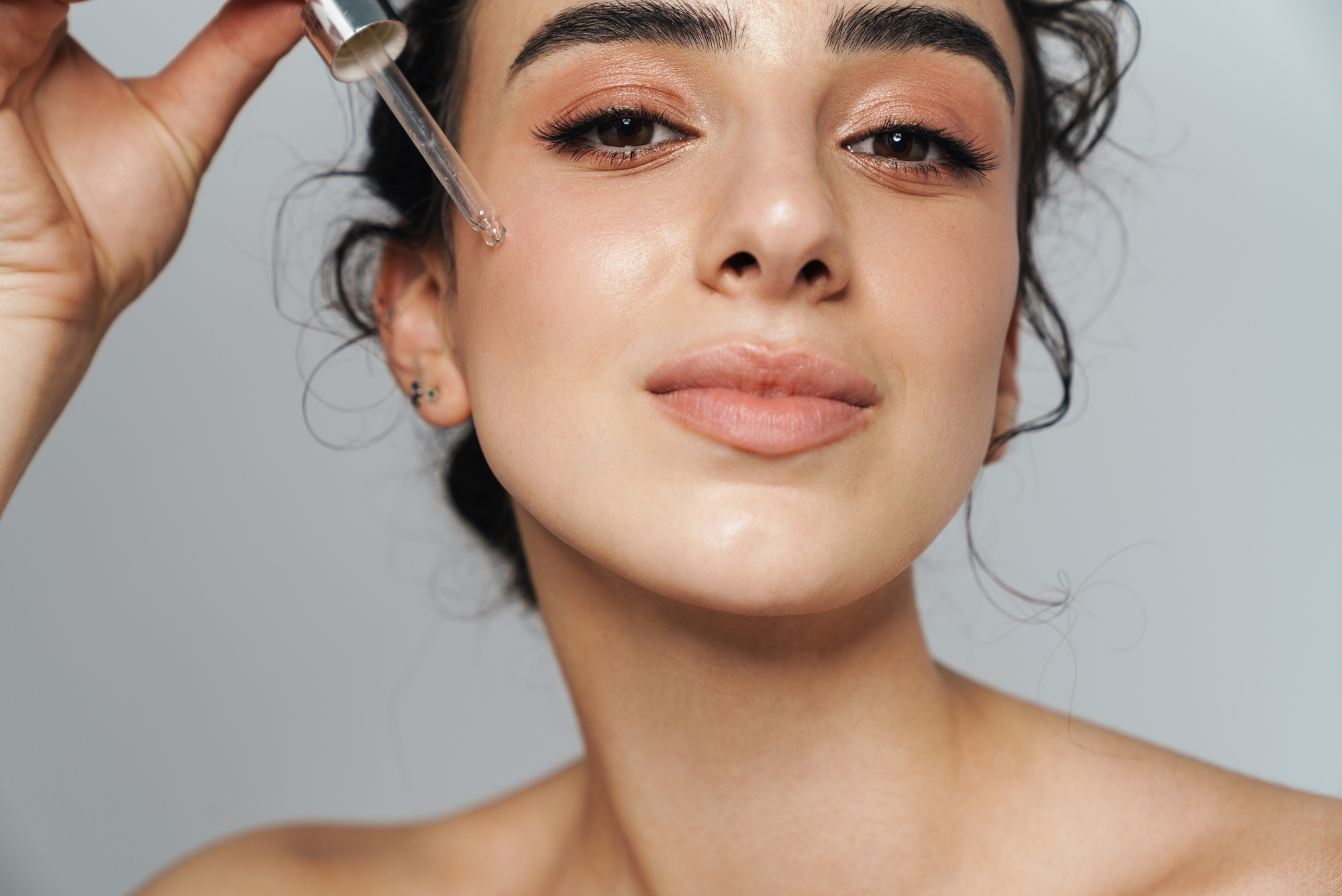 A woman with dark hair in a ponytail decides which serum to use with her LED light therapy and applies a drop to her face.